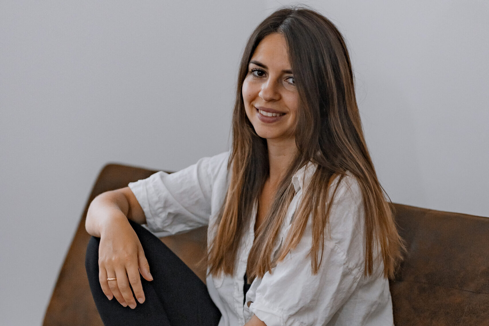 Frau sitzt mit schwarz-weißem Outfit auf einer Couch und lächelt freundlich in die Kamera.