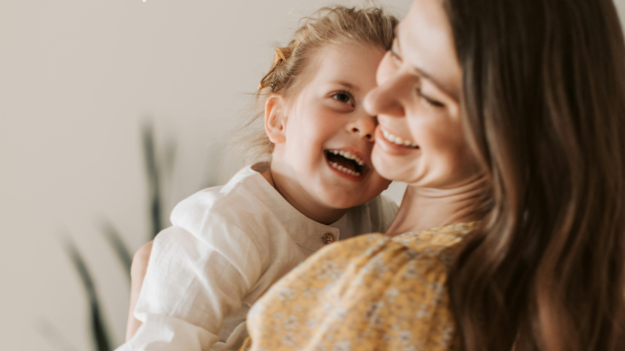 Mutter und Kind umarmen sich. Beide lachen, die Kleidung zeigt sich durch Beigetöne.